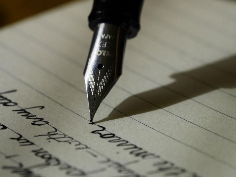 A fountain pen is writing on lined paper.