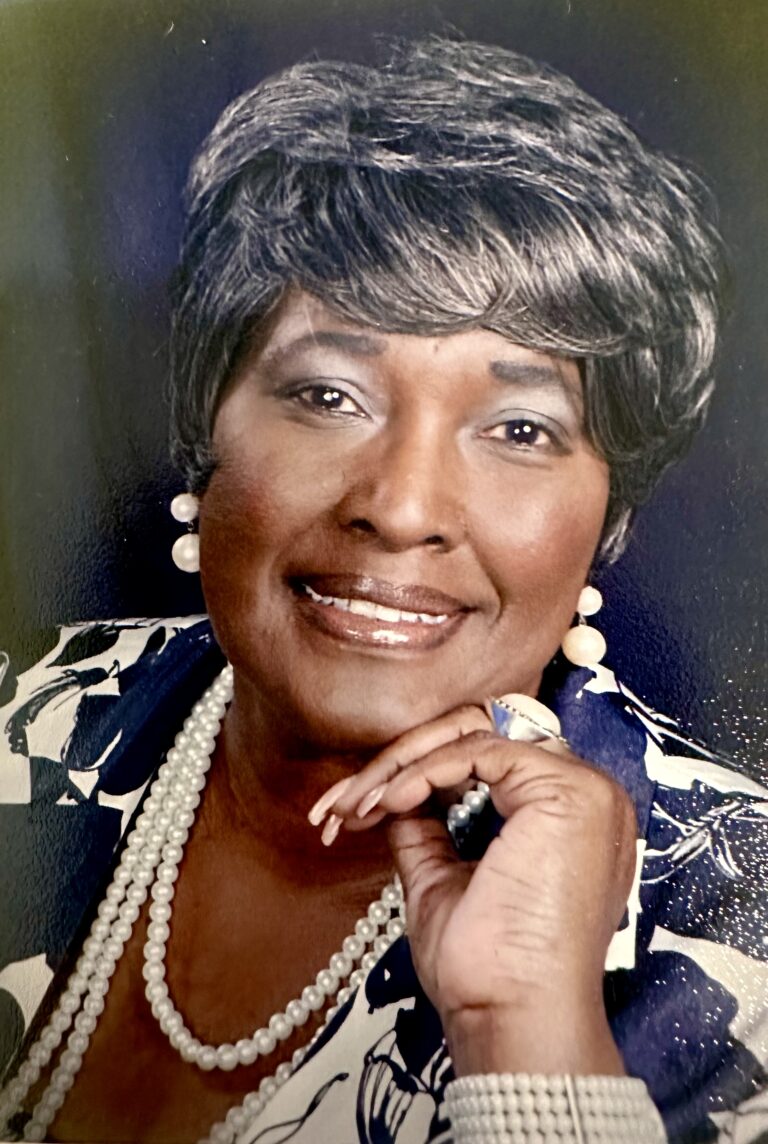 Smiling woman wearing pearl jewelry and suit.