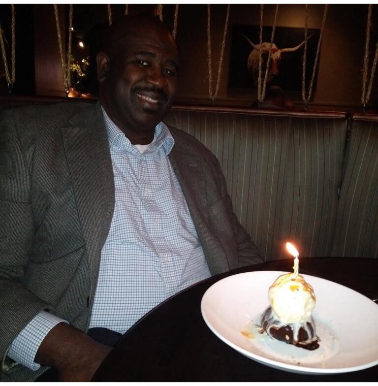 Man smiling with dessert and candle.